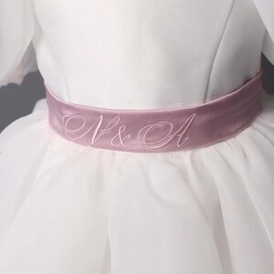 personalized first communion dress, custom flower girl dress, embroidered belt dress, first holy communion outfit, heirloom dress for girls, embroidered sash dress, ivory dress with monogram, white dress with big bow, special occasion dress girl, birthday dress with embroidered sash, wedding dress for young girls, flower girl dress with ribbon bow, baptism dress with embroidered belt