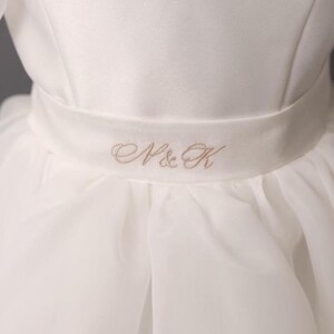personalized first communion dress, custom flower girl dress, embroidered belt dress, first holy communion outfit, heirloom dress for girls, embroidered sash dress, ivory dress with monogram, white dress with big bow, special occasion dress girl, birthday dress with embroidered sash, wedding dress for young girls, flower girl dress with ribbon bow, baptism dress with embroidered belt