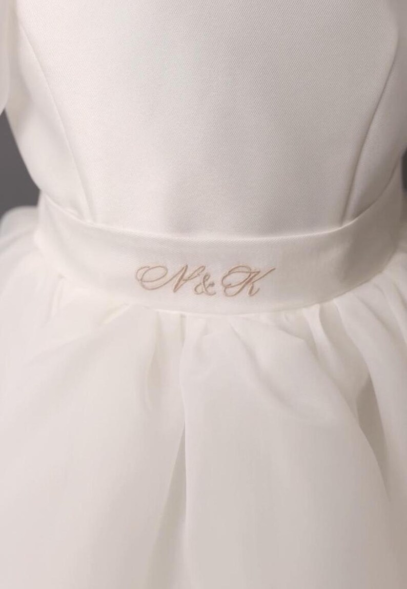 personalized first communion dress, custom flower girl dress, embroidered belt dress, first holy communion outfit, heirloom dress for girls, embroidered sash dress, ivory dress with monogram, white dress with big bow, special occasion dress girl, birthday dress with embroidered sash, wedding dress for young girls, flower girl dress with ribbon bow, baptism dress with embroidered belt