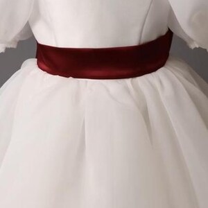 personalized first communion dress, custom flower girl dress, embroidered belt dress, first holy communion outfit, heirloom dress for girls, embroidered sash dress, ivory dress with monogram, white dress with big bow, special occasion dress girl, birthday dress with embroidered sash, wedding dress for young girls, flower girl dress with ribbon bow, baptism dress with embroidered belt