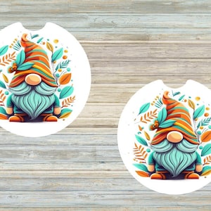 May include: Two round white coasters with a gnome design. Each coaster features a gnome with a blue beard, orange and yellow striped hat, and green leaves.