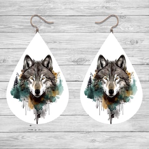 May include: A pair of teardrop-shaped earrings with a watercolor design of a wolf's face in a forest setting. The wolf's fur is gray and brown, and the forest is green and blue. The earrings are white and have a silver hook.