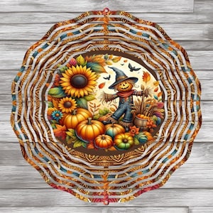 Op de afbeelding: Een decoratief, gelaagd, cirkelvormig herfstthema-ornament. Het midden toont een vogelverschrikker, pompoenen, zonnebloemen en herfstbladeren. De buitenste lagen hebben een herhalend patroon van oranje, bruin en blauw. Het ornament staat tegen een houten achtergrond.