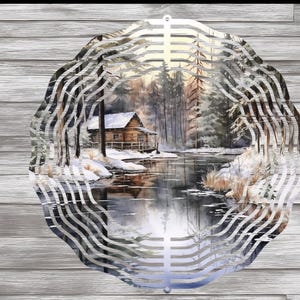 May include: A metal decorative wall hanging featuring a winter landscape scene. The artwork depicts a cabin by a snowy river surrounded by trees. The outer frame has a wavy, layered design. The background is a wooden texture.