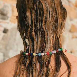 Könnte beinhalten: Eine Person mit langen, nassen, braunen Haaren trägt eine bunte Perlenkette. Die Perlen sind in verschiedenen Blautönen, Grün, Rosa, Gelb und Weiß.