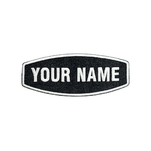 May include: A black embroidered patch with a white border and the text YOUR NAME in white capital letters. The patch has a horizontal, elongated hexagonal shape with rounded corners, featuring a dense, textured thread finish throughout.
