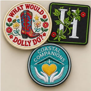 Pu&ograve; includere: Tre toppe ricamate: una toppa circolare color crema con uno stivale da cowboy rosso e il testo 'WHAT WOULD DOLLY DO?', una toppa quadrata nera con una lettera 'H' bianca intrecciata con viti verdi e fiori rossi, e una toppa circolare color ottanio con il testo 'COASTAL COMPANIONS' sopra due mani che tengono un cuore giallo.