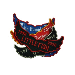 Peut inclure: Un ensemble de quatre patchs brodés représentant un oiseau stylisé avec les ailes déployées. Les patchs sont de différentes couleurs, notamment noir, rouge, bleu et jaune. Chaque patch est brodé d'une année et d'un nom, notamment "Little Fish", "Colin Humph", "Turner" et "2013".