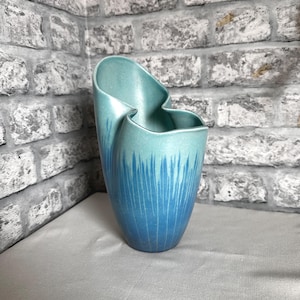 Könnte beinhalten: Eine Keramikvase mit asymmetrischem, gewelltem Rand und glatter Oberfläche. Die Farbe verläuft von einem hellen, blassen Türkis am oberen Rand zu einem tiefen, gesättigten Blau an der Basis, mit einem vertikalen, pinselartigen Muster.