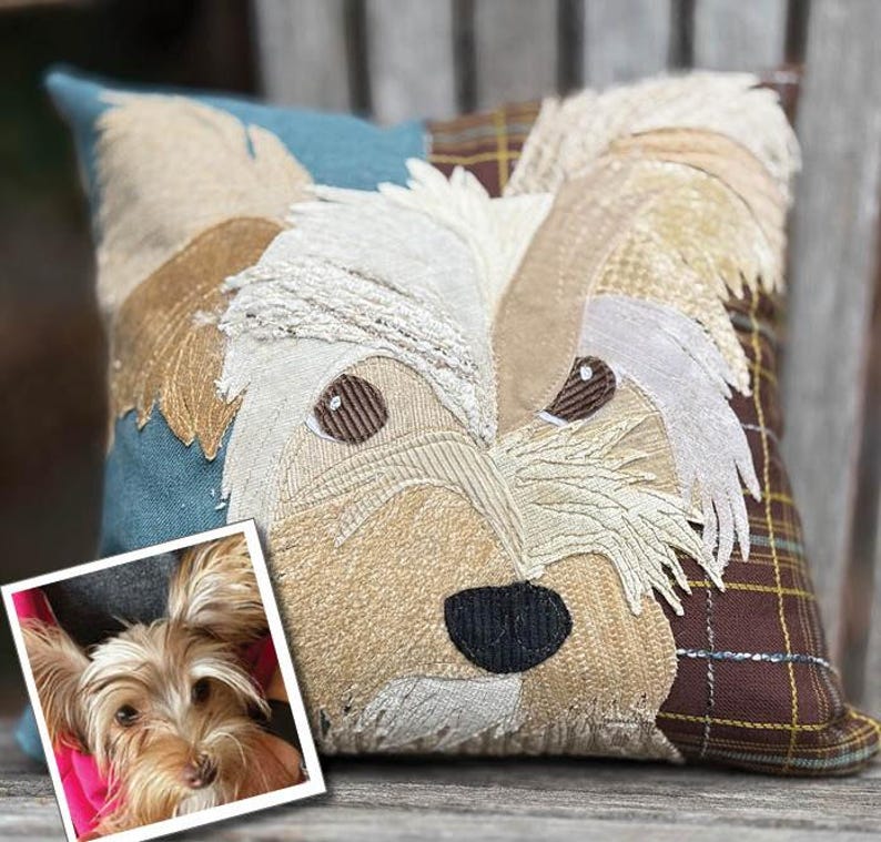 May include: Square decorative pillow featuring a dog's face. The pillow has a patchwork design with various textures and colors, including beige, brown, blue, and plaid. The dog's face is detailed with embroidered features and a black nose. A small photo of the dog is in the corner.