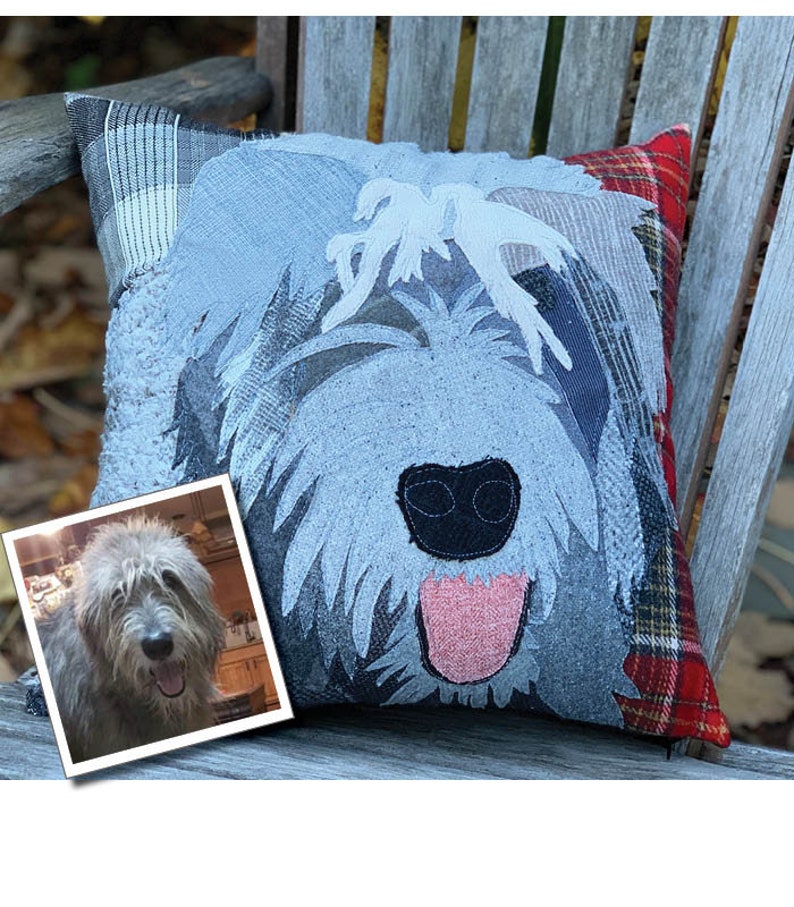 May include: A decorative square pillow featuring a dog face design. The pillow has a light blue and gray color scheme with a black nose and pink tongue. A framed photo of a dog is in the lower left corner. The pillow is placed on a wooden bench.