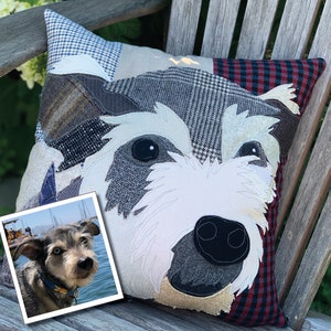 May include: A decorative dog-themed pillow with a patchwork design. The pillow features a dog's face with white, gray, and black details. The background is a mix of patterned fabrics in blue, gray, and red. A small photo of a dog is in the corner.