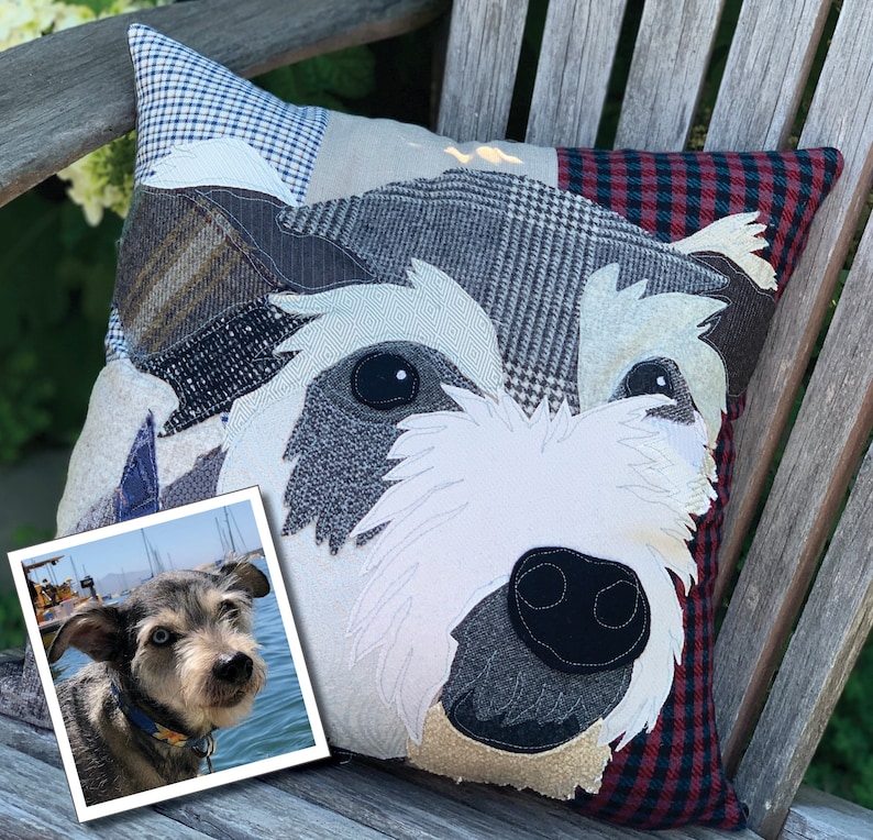 May include: A decorative dog-themed pillow with a patchwork design. The pillow features a dog's face with white, gray, and black details. The background is a mix of patterned fabrics in blue, gray, and red. A small photo of a dog is in the corner.