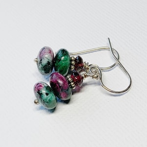 May include: Green and pink gemstone earrings with silver hooks. The earrings feature three round gemstones, two green and one pink, with a smaller red gemstone between each.