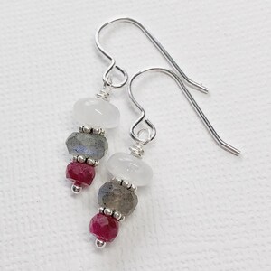May include: Silver dangle earrings with three beads each. The top bead is white, the middle bead is gray, and the bottom bead is red.