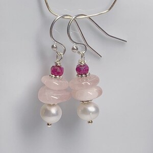 May include: Pink and white gemstone earrings with a pink ruby accent. The earrings are made with silver hooks and feature a layered design.
