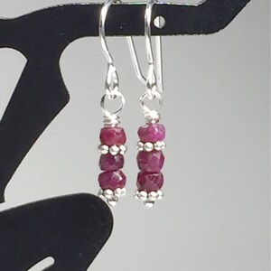 May include: A pair of silver earrings with three pink ruby beads on each earring.
