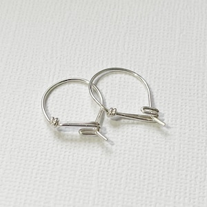 May include: A pair of small, silver hoop earrings. The hoops are made of thin wire and have a simple, minimalist design.