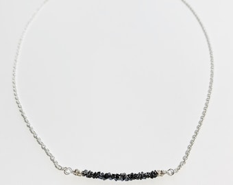 May include: A silver chain necklace with a row of black diamond chips.
