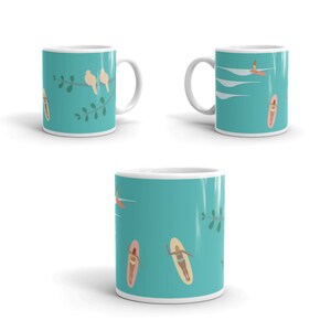 May include: White ceramic mug with a teal background featuring illustrations of birds on a branch and people surfing. The mug has a white handle and rim. The design wraps around the mug.