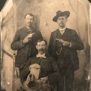 May include: Black and white photograph of three men posing with guns. The men are wearing suits and hats. The photo is likely from the late 1800s or early 1900s.