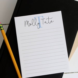 May include: A white notepad with blue lined paper and the text "Molly Tate" with a blue letter "T" in a larger font.