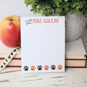May include: A white notepad with a black and orange paw print border. The notepad has the text "a note from MRS. GAULKE" at the top.