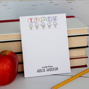 May include: A white notepad with a speech bubble design featuring the word "SPEECH" in rainbow colors. The notepad has a note that says "a note from JULIE HOEFER".