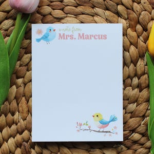 May include: A blue and yellow bird illustration on a white notepad with the text "a note from Mrs. Marcus". The notepad is on a woven brown background with two tulips, one pink and one yellow.
