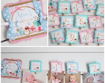 May include: Alice's First Year banner with a pink and blue color scheme. The banner features a whimsical Alice in Wonderland theme with images of the Mad Hatter, the Queen of Hearts, and a pocket watch. The banner is decorated with gold glitter and blue and white polka dot bows.