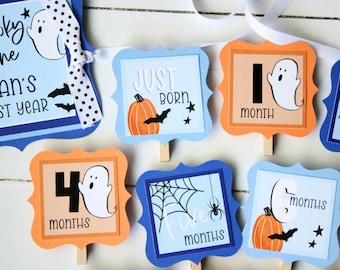 May include: A Halloween-themed baby milestone banner with orange and blue squares. Each square features a ghost, pumpkin, bat, spider, and the number of months. The banner reads "Spooky One Cian's First Year", "Just Born", "1 Month", "4 Months", "Five Months", and "6 Months".
