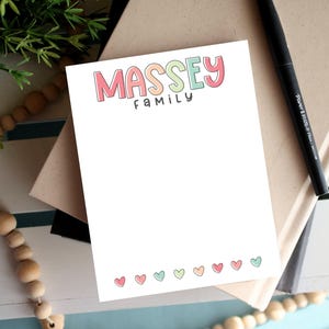May include: A white notepad with the text "MASSEY FAMILY" in rainbow colors. The notepad has a row of small pink hearts at the bottom.