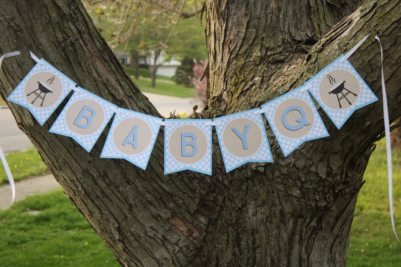 May include: A blue and brown banner with the text "BABY Q" and a small grill icon on each end. The banner is hanging from a tree branch.