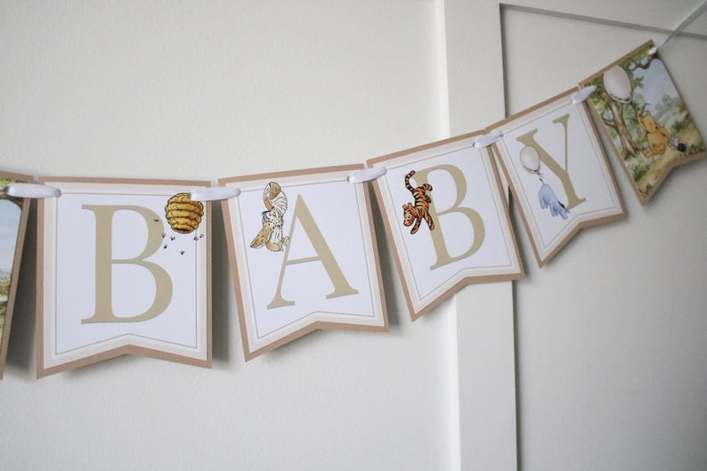 May include: A Winnie the Pooh themed baby shower banner with the word "BABY" in white letters on a brown background. Each letter has a different Winnie the Pooh character or object on it.