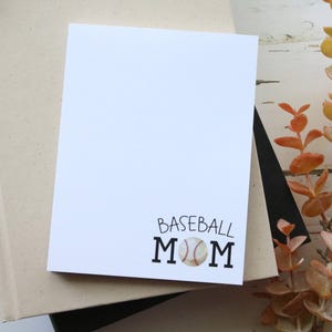 May include: A white card with the text "Baseball Mom" and a baseball graphic. The card is sitting on top of a brown book.
