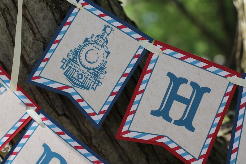 May include: A blue and red striped banner with the letters "H" and a vintage train engine illustration. The banner is made of paper and has a rustic look.
