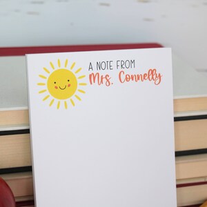 Puede incluir: Un bloc de notas blanco con un sol amarillo sonriente y el texto "A note from Mrs. Connelly" impreso en &eacute;l.