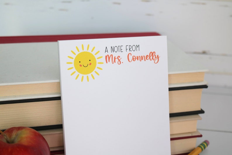 Puede incluir: Un bloc de notas blanco con un sol amarillo sonriente y el texto "A note from Mrs. Connelly" impreso en &eacute;l.