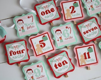 Könnte beinhalten: Ein Set mit 11 weihnachtlichen Monatskarten für ein Baby. Jede Karte zeigt eine andere Zahl von 1 bis 11 mit einem Design aus Weihnachtsmann, Lebkuchenmann oder Zuckerstange. Die Karten sind in den Farben Rot, Grün und Weiß verziert.