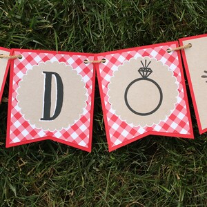 May include: A red and white gingham banner with the words "DO" in black letters. The "O" is decorated with a ring and diamond.