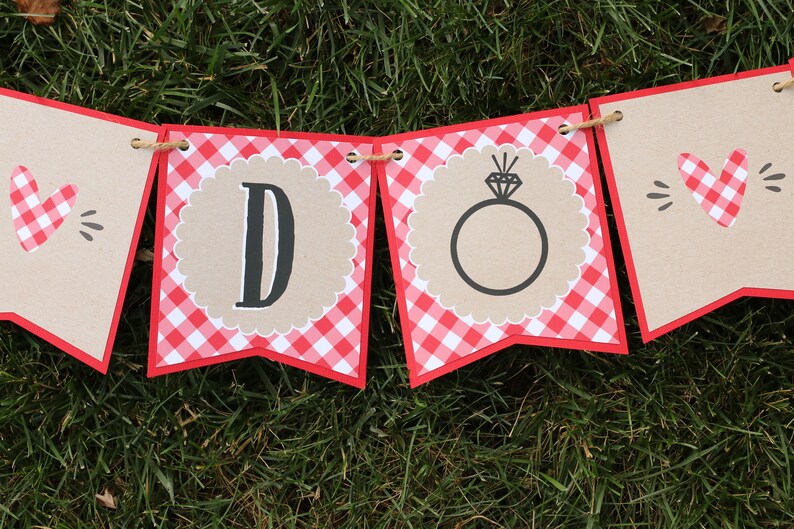 May include: A red and white gingham banner with the words "DO" in black letters. The "O" is decorated with a ring and diamond.