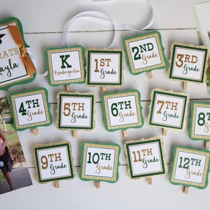 May include: Green and gold graduation signs with glitter and white text. The signs say "Congrats Mikayla", "Kindergarten", "1st Grade", "2nd Grade", "3rd Grade", "4th Grade", "5th Grade", "6th Grade", "7th Grade", "8th Grade", "9th Grade", "10th Grade", "11th Grade", and "12th Grade".