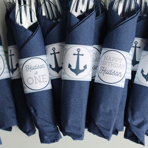 May include: Blue and white nautical themed napkin rings with an anchor design and the text "Happy Birthday Hudson" and "Hudson is One".