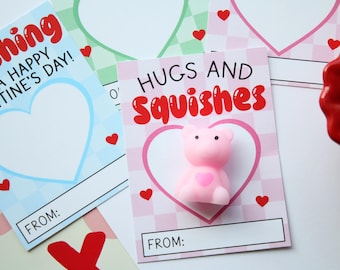 Op de afbeelding: Twee Valentijnsdagkaarten met roze en blauwe geruite achtergronden. De kaarten hebben een hartvorm en de tekst "Wishing you a happy Valentine's Day!" en "Hugs and Squishes". De kaart met de tekst "Hugs and Squishes" heeft een roze, beer-vormig squishy speelgoed erop.