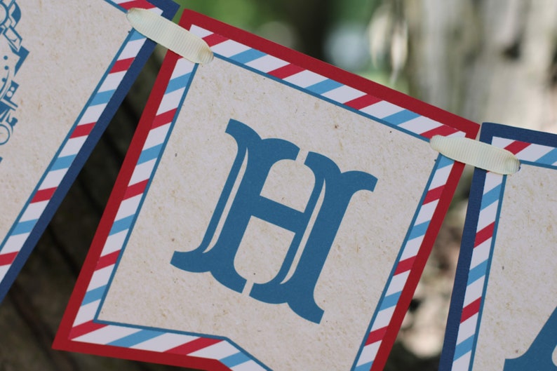 May include: A red, white, and blue striped banner with the letter "H" printed in blue. The banner is made of paper and has a rustic look.