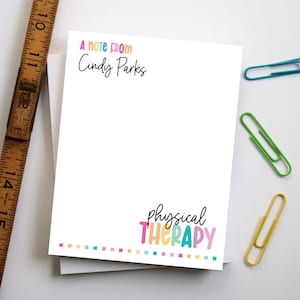 May include: White notepad with the text "A note from Cindy Parks" in black and colorful text that says "physical THERAPY". The notepad has a colorful dotted border. Includes a wooden ruler and colorful paperclips.