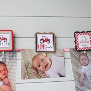 May include: A red and white baby milestone banner with pictures of a baby at different ages. The banner features a red tractor design and the words "NEWBORN", "ONE month", and "2 MONTHS".