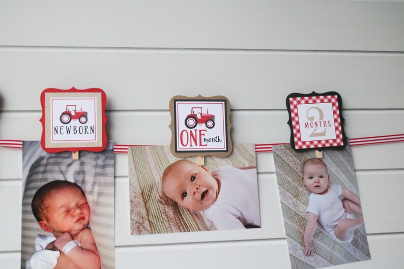 May include: A red and white baby milestone banner with pictures of a baby at different ages. The banner features a red tractor design and the words "NEWBORN", "ONE month", and "2 MONTHS".