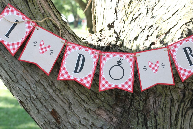 May include: A red and white gingham banner with the words "I Do" in black letters. The banner is decorated with hearts and a ring.
