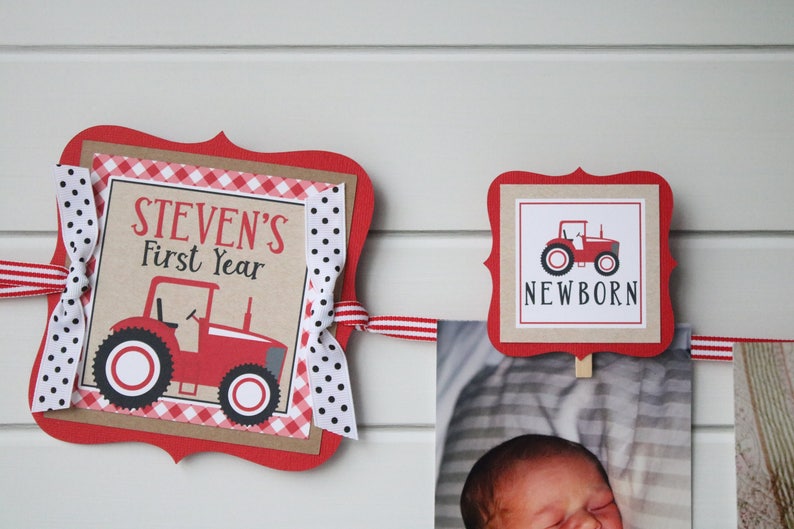 May include: Red and white tractor themed banner with the text "STEVEN'S First Year" and "NEWBORN". The banner is decorated with red and white gingham and polka dot ribbon.